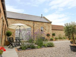 a patio with an umbrella and flowers in front of a building at Wallerthwaite Barn Cottage in Harrogate