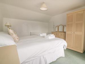 a bedroom with a large white bed and a cabinet at Honeysuckle Cottage in St Austell