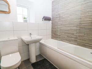 a white bathroom with a sink and a toilet and a bath tub at Ysgubor Llwyd in Holyhead