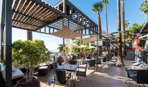 a patio with tables and chairs and palm trees at The Harbour Club in Acantilado de los Gigantes