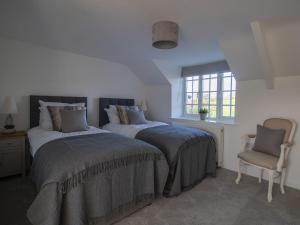 a bedroom with two beds and a chair and a window at Willowbrook Cottage in Bridport