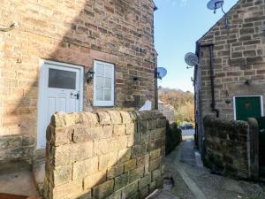 a stone building with a white door and a brick wall at Milford Cottage in Belper