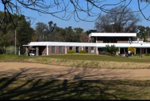 a building in front of a field with a dirt road at Estudio hindu club in Don Torcuato