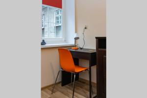 - un bureau avec une chaise orange à côté d'une fenêtre dans l'établissement Apartament Brama Chlebnicka, à Gdańsk