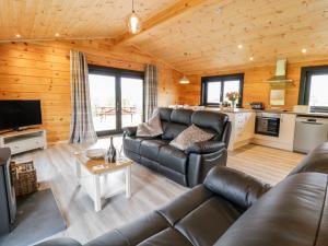 a living room with a leather couch and a kitchen at Bryn Eiddon Log Cabin in Machynlleth