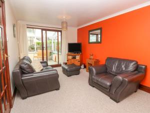 a living room with leather furniture and an orange wall at Mossley Cottage in Penzance