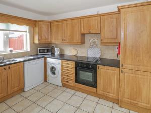 cocina con armarios de madera, lavadora y secadora en Duffy's Cottage en Ballymote