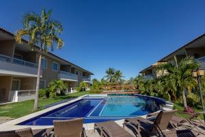 a swimming pool in a resort with chairs and palm trees at Guarajuba Village Verano A01, térreo - GUARAJUBA TEMPORADA, viva mais de uma experiência de hospedagem conosco! in Guarajuba