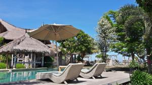 a group of chairs and an umbrella next to a pool at Puri Air Beach Resort & Spa in Gili Air