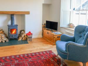 sala de estar con chimenea, 2 sillas y TV en Howgill Cottage en Sedbergh