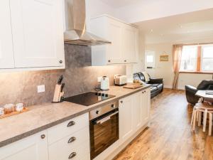 a kitchen with white cabinets and a living room at Glebe Cottage in Dumfries