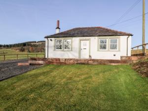 a small white house with a grass yard at Glebe Cottage in Dumfries