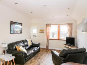 a living room with a leather couch and a tv at Glebe Cottage in Dumfries