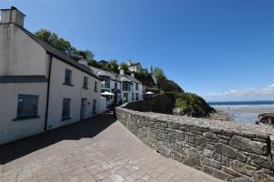 a street with a stone wall and houses and the ocean at Beach Cottage in Little Haven