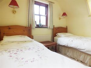 a bedroom with two beds and a window and a table at Cockshead Cottage in Saint Dogmaels