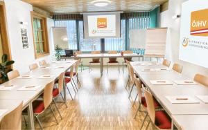 una sala conferenze con tavoli, sedie e schermo di Jugend- und Familiengästehaus Cap Wörth a Velden am Wörthersee
