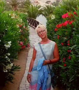 an older woman standing in a garden with flowers at Hotel garni & Oma's Heuhotel 'Pension zur Galerie' in Barby