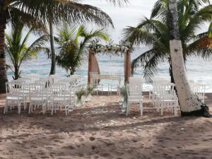 una boda en la playa con sillas blancas y palmeras en Villa Mar, Juan Dolio en Juan Dolio