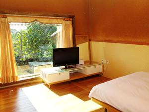a bedroom with a bed and a television and a window at Angkure Pension in Seogwipo