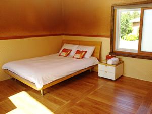 a bedroom with a bed with two pillows and a window at Angkure Pension in Seogwipo