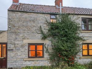 a stone house with orange windows and a tree at Summerfield Farm Cottage in York