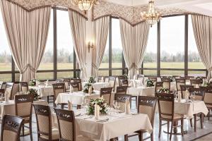 un comedor con mesas y sillas blancas y ventanas en Boutique Odyseja & Spa, en Ciechocinek