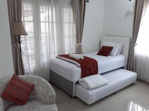 a white bedroom with two beds and a chair at Surokarsan 9 House Yogyakarta in Yogyakarta