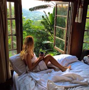 una mujer sentada en una cama mirando por la ventana en The Den of the Treehouse, KINABALU Farm, en The Pocket