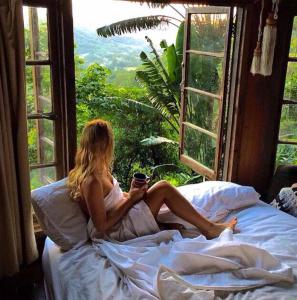 a woman sitting on a bed looking out a window at The Den of the Treehouse, KINABALU Farm in The Pocket