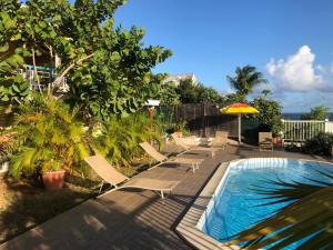 a swimming pool with lounge chairs and an umbrella at Mango Sea -Villa "Maracudja" et appartement "Jojoba" avec piscine & vue sur les îles in Saint-François