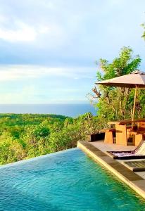 a swimming pool with an umbrella and chairs and the ocean at OCEANNA - Uluwatu, Bali in Uluwatu