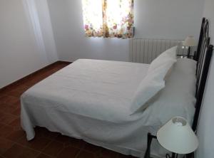 Una cama con sábanas blancas y almohadas en un dormitorio en Alojamiento Rural El Orégano, en Campillos