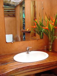 a bathroom sink with a mirror and flowers in it at Vanira Lodge in Teahupoo