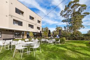 a group of tables and chairs in the grass in front of a building at Miramare Gardens Boutique Accommodation in Terrey Hills