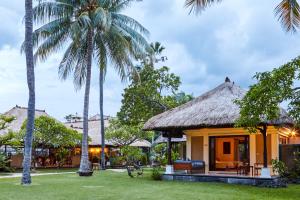 a house with a thatched roof and palm trees at Puri Bagus Lovina in Lovina