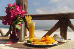 a plate of fruit and a drink on a table on the beach at Isla Bonita Zanzibar Beach Resort in Matemwe