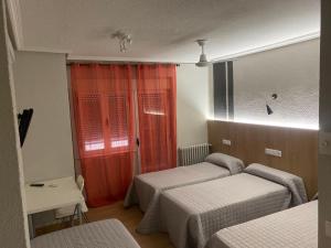 1 dormitorio con 2 camas y cortina roja en Hostal Uría, en Salamanca