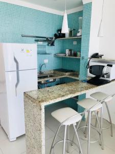 uma cozinha com um frigorífico branco e bancos brancos em Flats Boulevard Center Pitangueiras no Guarujá