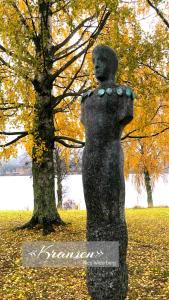 Una statua di una donna in piedi accanto a un albero. di Hurdalsjøen Hotel a Hurdal