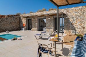 eine Terrasse mit einem Tisch, Stühlen und einem Pool in der Unterkunft Varkotopi Villas in Agios Pavlos