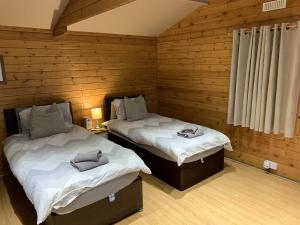 two beds in a room with wooden walls at Southernwood - Garden Lodge 2 in Didcot