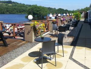 une rangée de tables et de chaises à côté de l'eau dans l'établissement The Inn on the Loch, à Castle Douglas