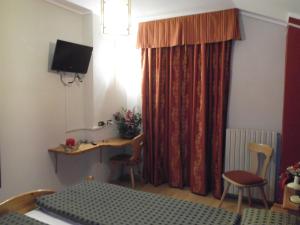 Cette chambre comprend un lit, un bureau et une télévision. dans l'établissement Hotel Adele, à Livigno