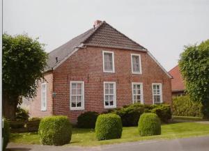 a red brick house with white windows and bushes at Ferienhof Welsch Wohnung 2 in Großefehn 