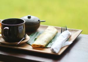 een bord eten met een kopje en een vork en mes bij Pondok Muwa Guest House in Ubud