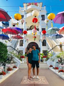 Un uomo e una donna in piedi di fronte a un palazzo con degli ombrelloni di Timothy Homestay Hue a Hue