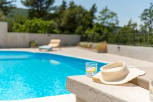 un sombrero de paja y un vaso de agua junto a la piscina en Newly refreshed property JOVI-relaxing, fenced, private, heated pool & view, en Tugare