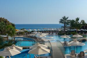 Melissi Beach Hotel & Spa في أيا نابا: حمام سباحة مع المظلات والكراسي البيضاء والمحيط