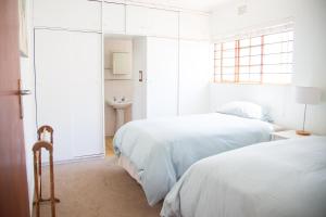 a white bedroom with two beds and a window at Green Nook in Plettenberg Bay