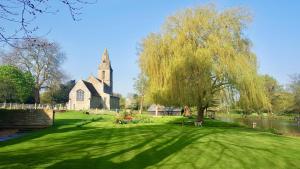 a church with a tree in the middle of a field at River Nene Cottages in Water Newton